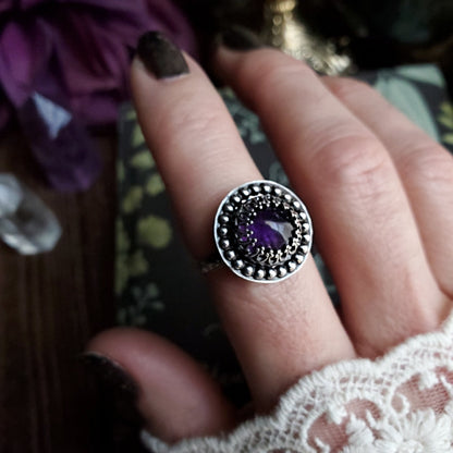 a woman’s hand holding a ring with a purple stone