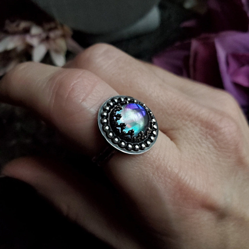 a person’s hand holding a ring with a rainbow colored stone