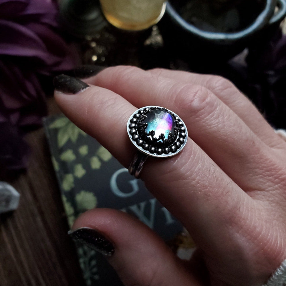 a person holding a ring with a rainbow colored stone