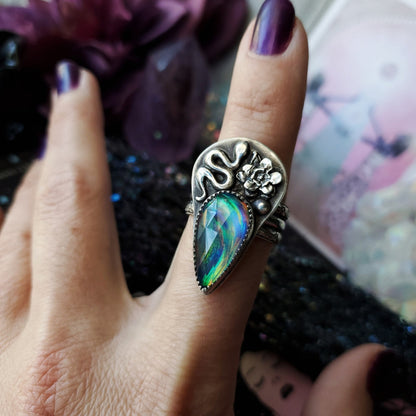 a woman’s hand with a ring with a rainbow colored stone