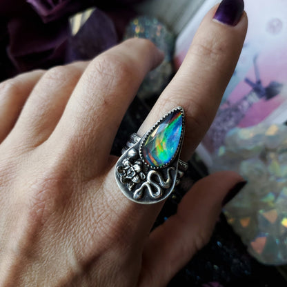 a woman’s hand holding a ring with a rainbow colored stone