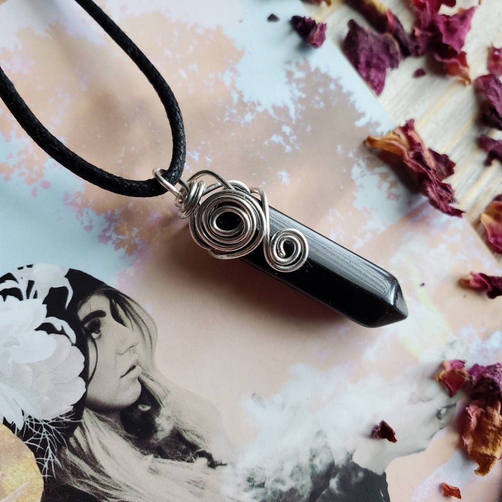 a black stone pendant with a spiral design on a black cord necklace