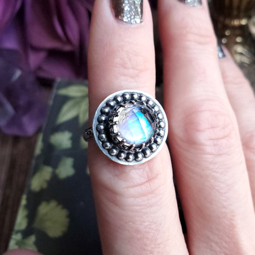 a woman’s hand holding a ring with a rainbow colored stone