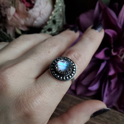 a woman’s hand holding a ring with a rainbow colored stone