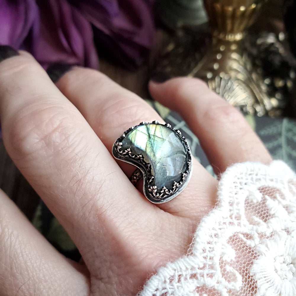 a woman’s hand holding a ring with a green and white stone