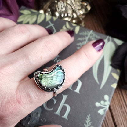 a woman’s hand holding a ring with a green stone