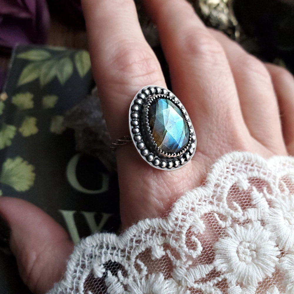 a woman’s hand holding a ring with a blue stone