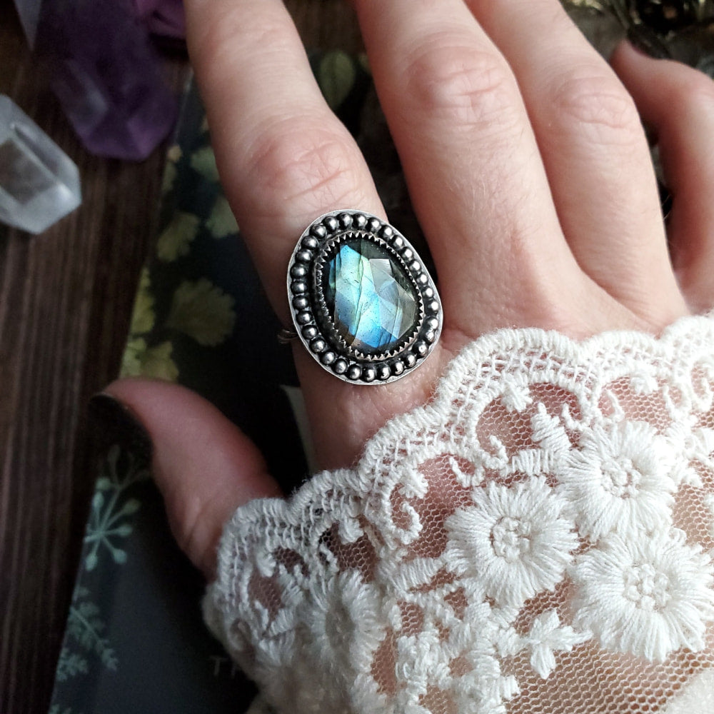 a woman’s hand holding a ring with a blue stone