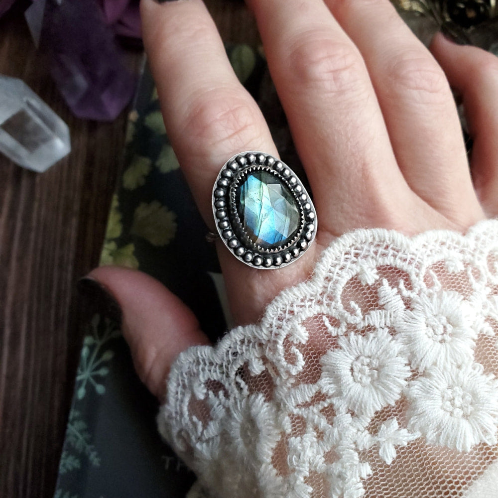 a woman’s hand holding a ring with a blue stone