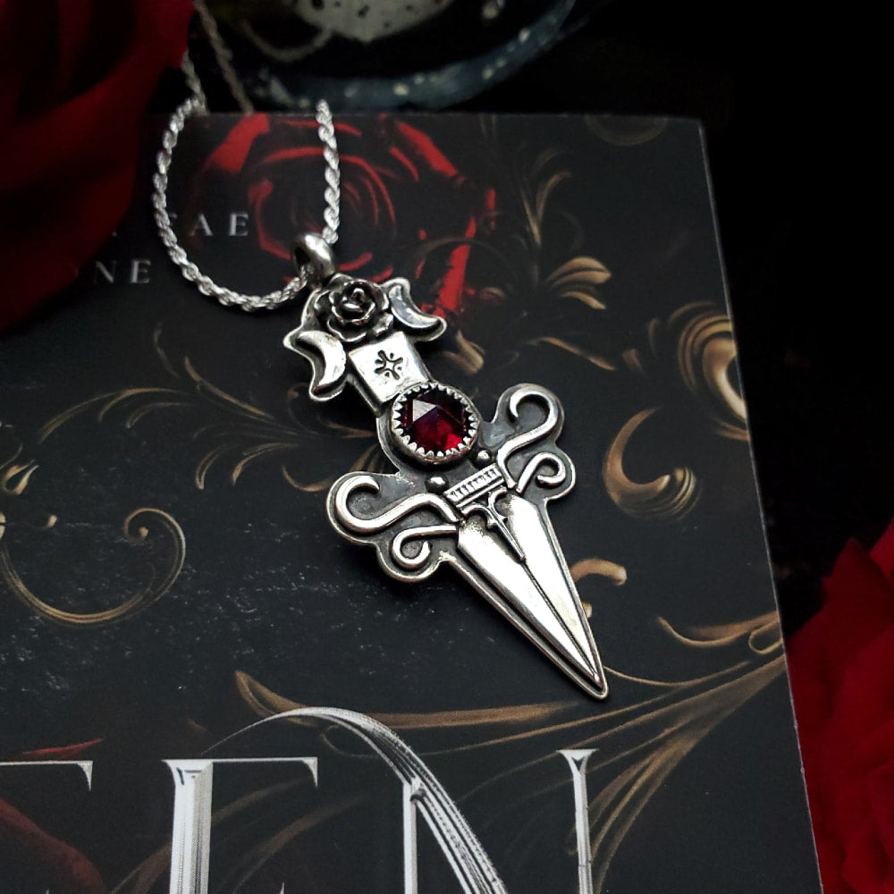 a dagger pendant with a red stone on it