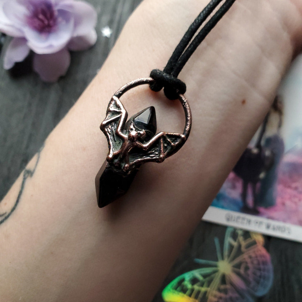 Bat-shaped pendant necklace with outstretched wings on a cord.