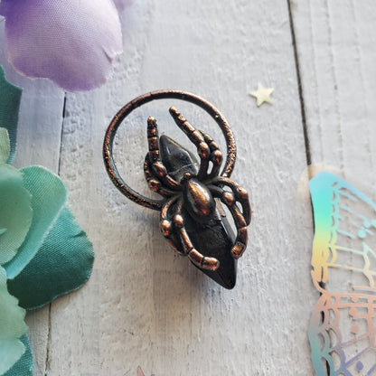 Bronze-colored spider-shaped decorative piece with a circular attachment.