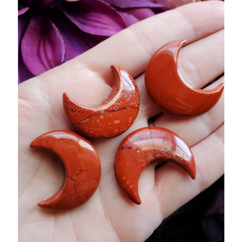 Hand holding three red jasper crescent moon crystals for necklace or individual use