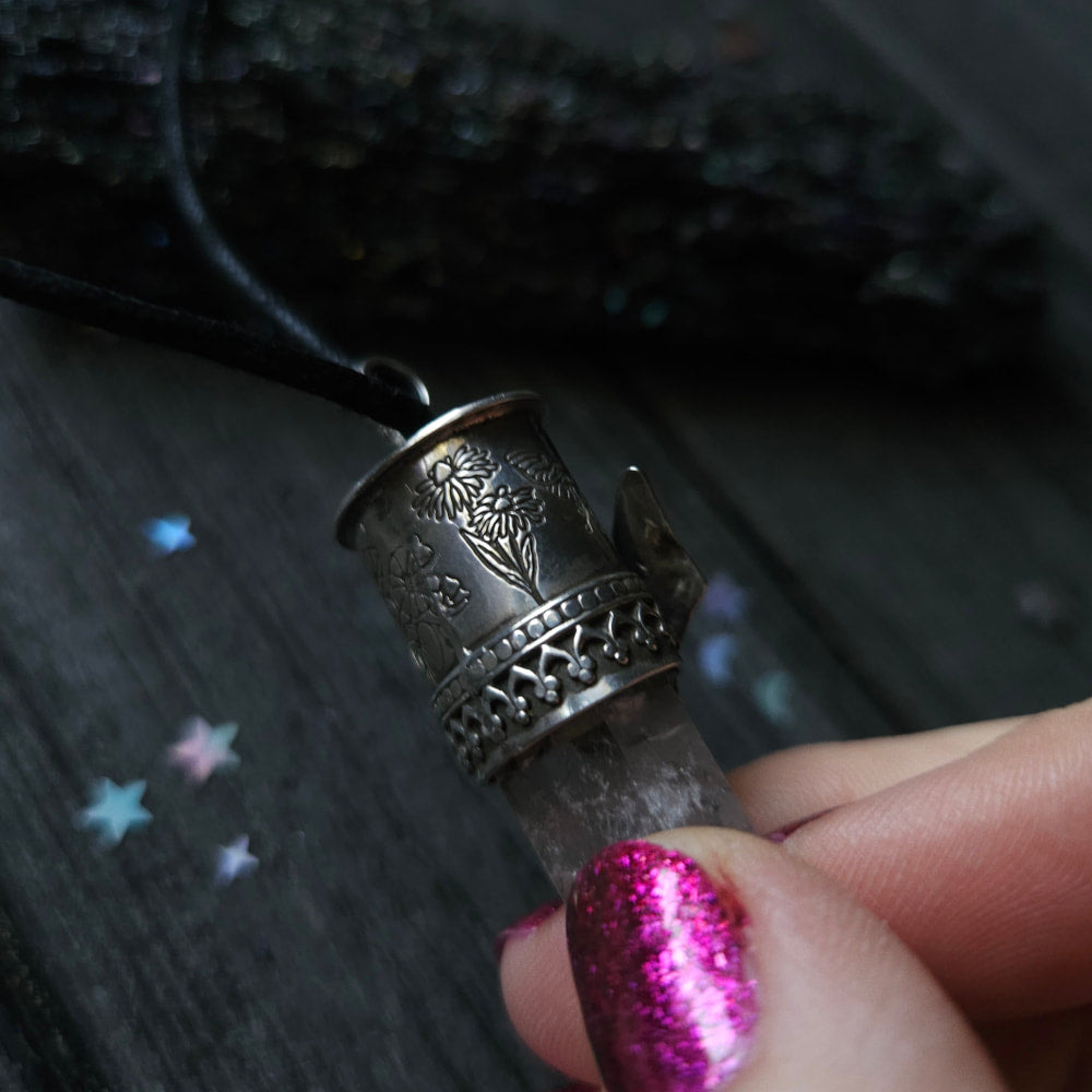 Ornate silver thimble pendant on a black cord held by a finger with sparkly pink nail polish.