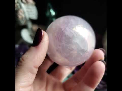 A hand rotating a rose quartz crystal sphere.